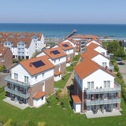 Ostseeresidenz Schönberger Strand, Aufnahme von oben, Ansicht der kompletten Anlage Ostseeresidenz Schönberger Strand mit den 6 Häusern, drumherum grüne Flächen und weitere Häuser, im Hintergrund Ostsee mit Seebrücke