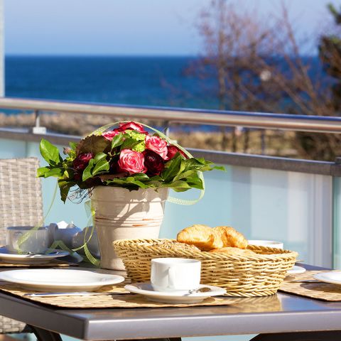 Penthouses Ostseeresidenz Schönberger Strand, Balkon, Nahaufnahme Tisch, Tisch ist mit Frühstück eingedeckt, Blumenvase mit Strauß, Blick vom Balkon auf die Ostsee