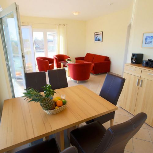 Penthouse Ostseeresidenz Schönberger Strand, Wohn- und Essbereich, Sitzecke mit Sofa und drei Sesseln, Essbereich Tisch und 6 Stühle, Sideboard mit Musikanlage, auf dem Tisch Obstkorb