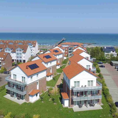 Ostseeresidenz Schönberger Strand, Aufnahme von oben, Ansicht der kompletten Anlage Ostseeresidenz Schönberger Strand mit den 6 Häusern, drumherum grüne Flächen und weitere Häuser, im Hintergrund Ostsee mit Seebrücke