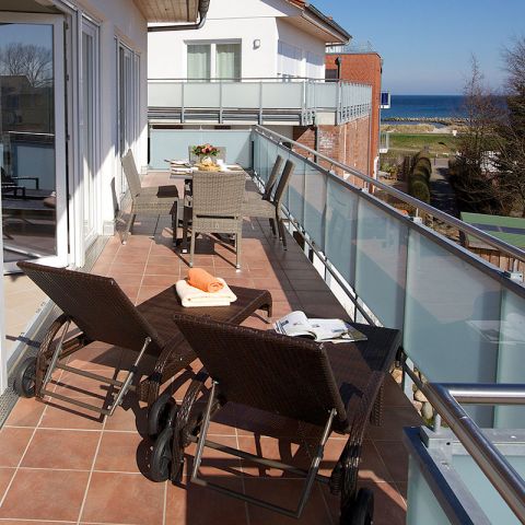 Penthouses Ostseeresidenz Schönberger Strand, Balkon mit zwei Rattanliegen sowie sechs Rattanstühle und Tisch, Tisch ist mit Frühstück eingedeckt, Blick vom Balkon auf die Ostsee