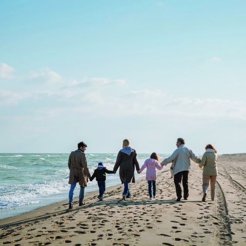 Umgebung Ostseeresidenz Schönberger Strand, 6 Personen, Familie Hand in Hand von hinten gehen am Strand spazieren, links Ostsee mit Wellen