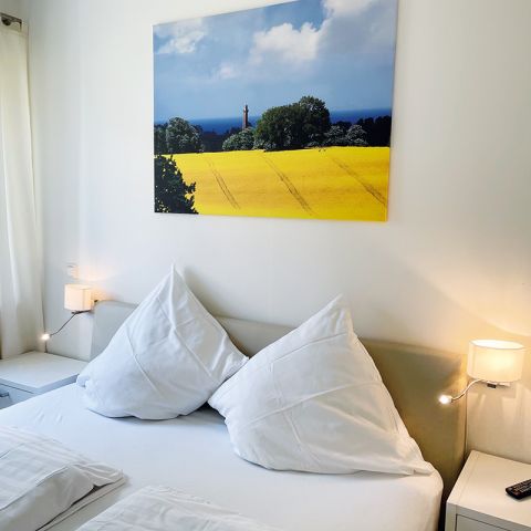 Ferienwohnung Ostseeresidenz Schönberger Strand, Ausschnitt Schlafzimmer mit Bett, links und rechts Nachttische sowie Lampen an der Wand, über dem Bett Leinwand mit Rapsfeldmotiv